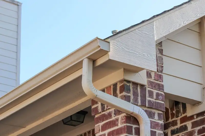 Close-up of seamless aluminum gutter and downspout installation on a brick home with soffit and fascia detail